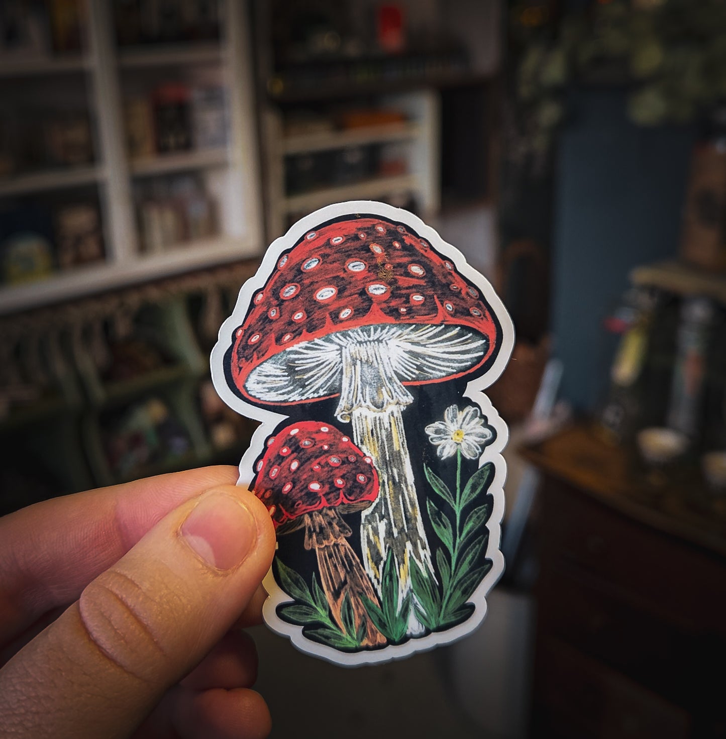 Sticker of red mushrooms held by a hand in a blurred indoor setting